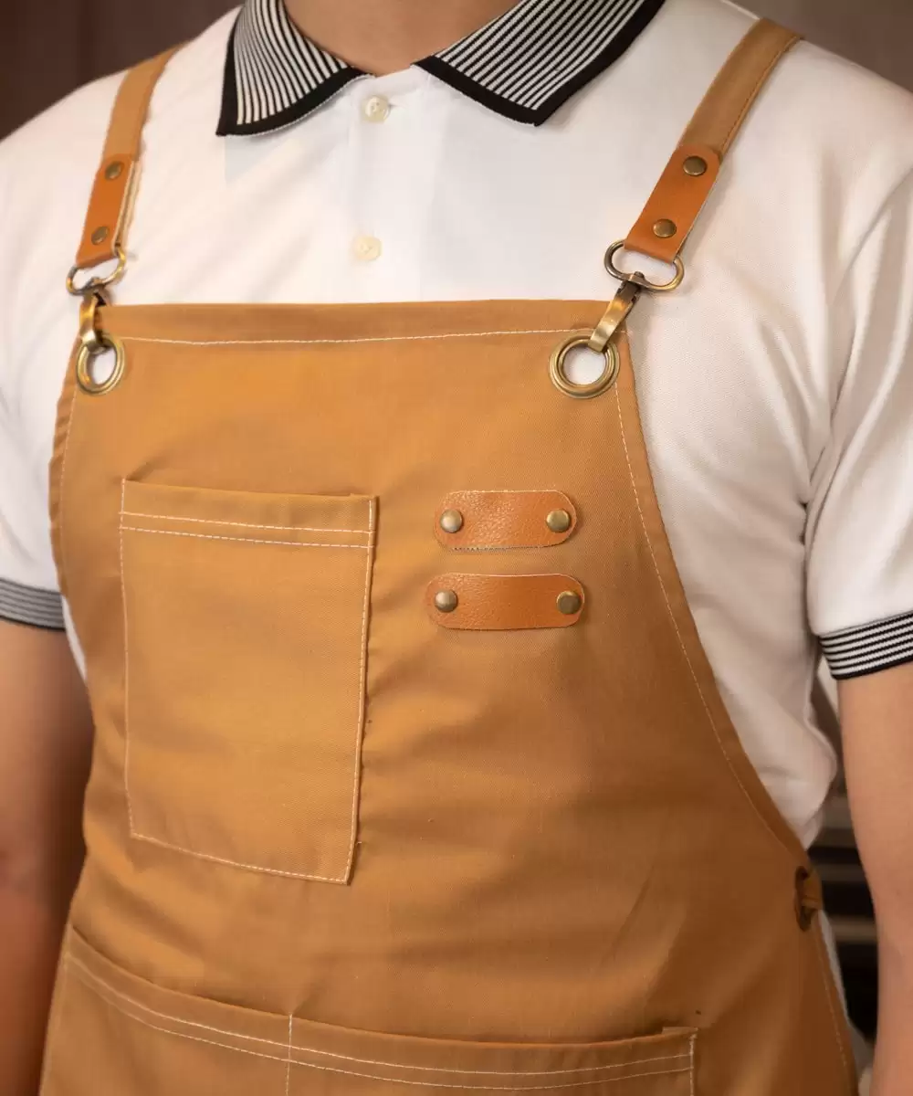 Đồng phục tạp dề màu be gắn chi tiết trên ngực được thiết kế dáng dài có nhiều bao phía trước